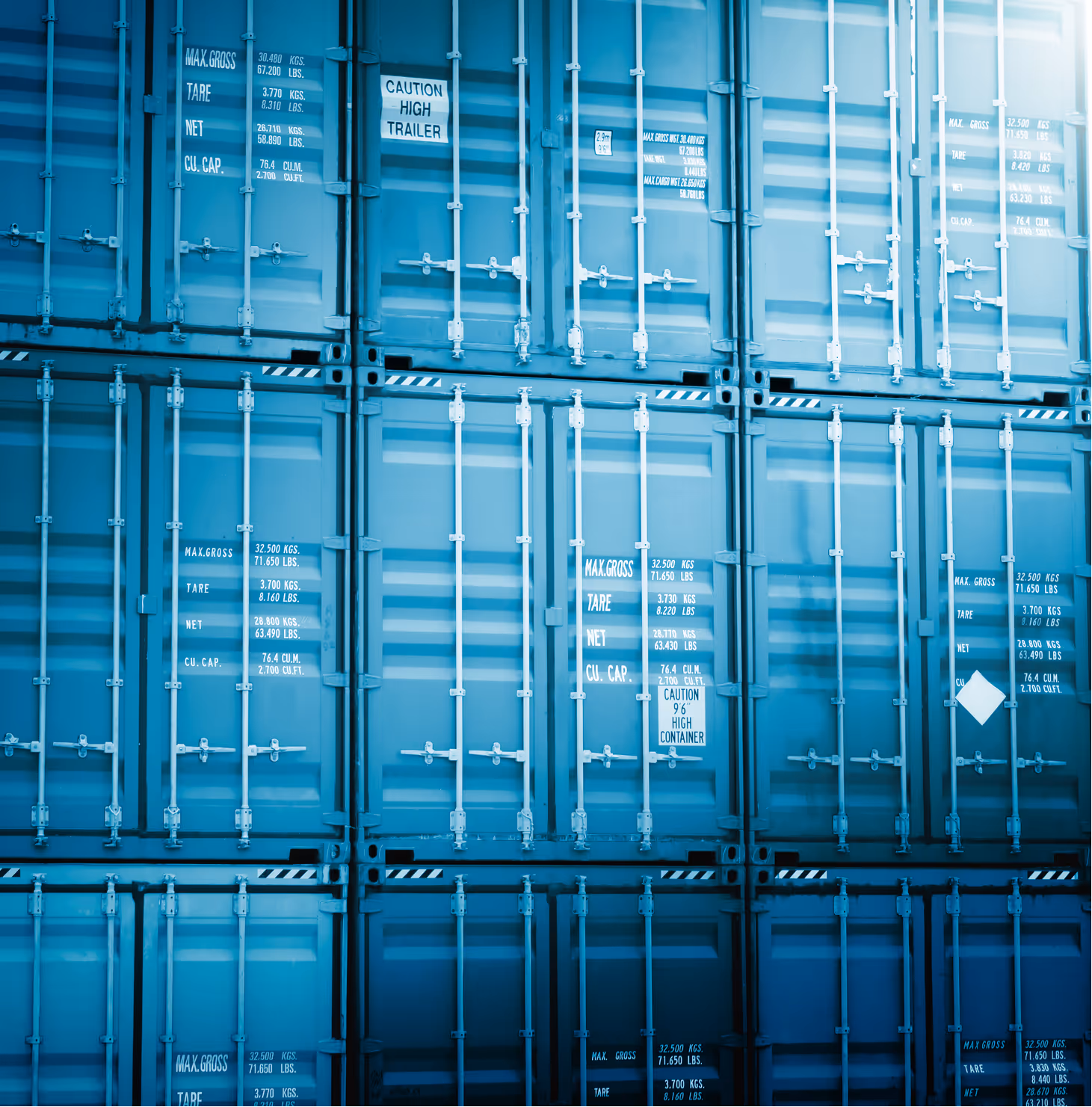 Stacked blue shipping containers with metal locking bars and white caution and weight markings.